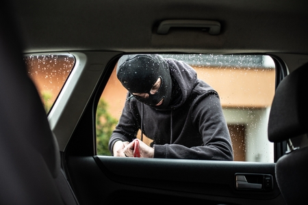 Car thief in a balaclava is trying to break into a car using a crowbarの写真素材