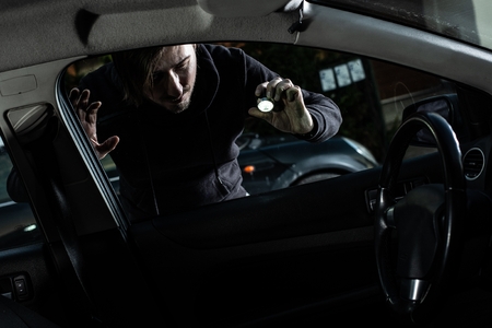 Masked thief in a balaclava looking to car interior with flashlightの写真素材