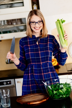 Woman with celery and knife in kitchen. Woman in kitchen. Female preparing delicious healthy fruit and vegetable smoothieの写真素材