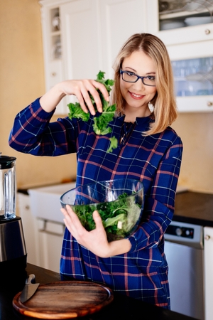 Young pregnant woman mixing green kale in a glass bowl in kitchen. Woman in kitchen. Female preparing delicious healthy fruit and vegetable smoothieの写真素材