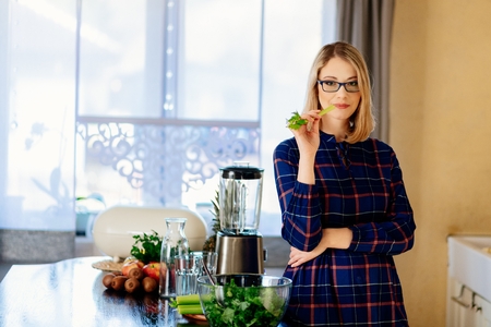 Pregnant woman eating green celery in kitchen. Woman in kitchen. Female preparing delicious healthy fruit and vegetable smoothieの写真素材