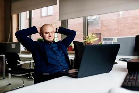 Relaxed man working in office on laptop computer. Young businessman in officeの写真素材
