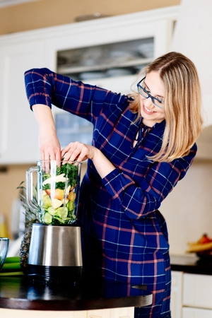 Woman putting fruits and vegetables into the eletrical blender. Woman preparing delicious healthy smoothieの写真素材