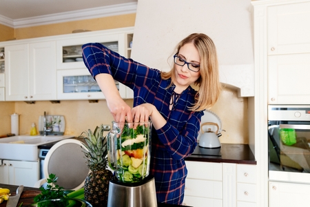 Woman putting fruits and vegetables into the eletrical blender. Woman preparing delicious healthy smoothieの写真素材