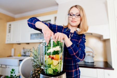 Woman putting fruits and vegetables into the eletrical blender. Woman preparing delicious healthy smoothieの写真素材