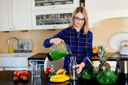 Young happy pregnant woman pouring green smoothie to glass cup. Fresh healthy vegan foodの写真素材