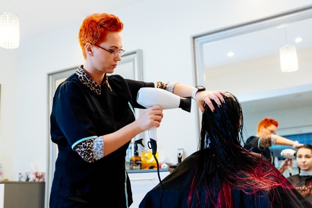 Woman hairdresser drying young woman customer hair in salon. Female in hairdresser salon
