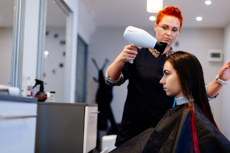Hairdresser drying customer hair with hair dryer. Woman in beauty hair salonの写真素材