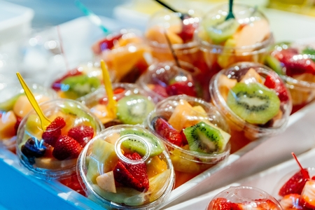Plastic cups with delicious fruits for sale. Kiwi, pineapple and other juicy fruits in plastic cup. Takeaway fruitsの写真素材