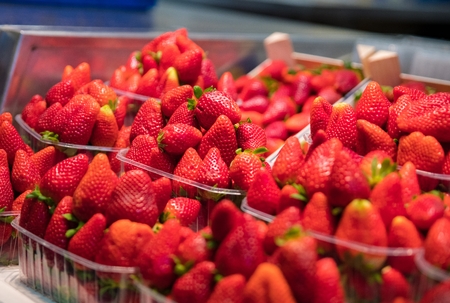 Red delicious strawberries in plastic baskets for sale on market stallの写真素材