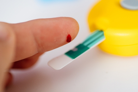 Blood test with glucose meter. Man doing glucose blood test with lancet hand prick and glucose meterの写真素材
