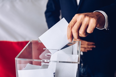 Man throwing his vote into the ballot box. Polish flag in the background. Elections to the Polish Parliament.の写真素材
