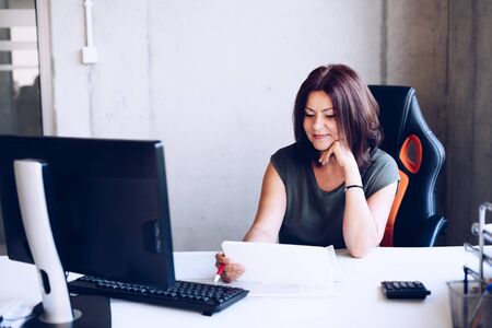 Happy 40s middle-aged brunette woman working in the office with computerの写真素材