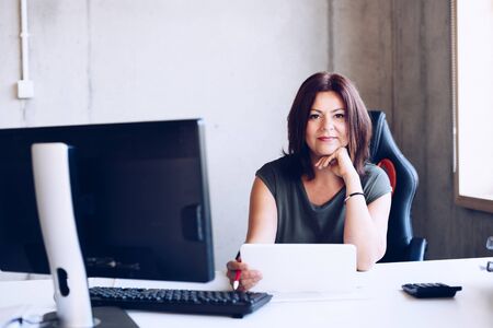 Happy 40s middle-aged brunette woman working in the office with computerの写真素材