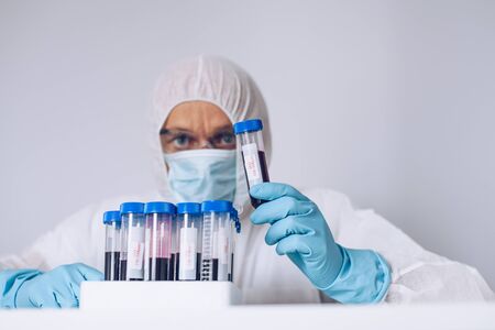 Scientist in protective suit holding test tube with blood