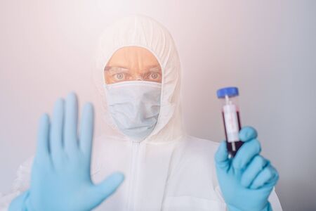 Scientist in protective suit holding test tube with bloodの写真素材