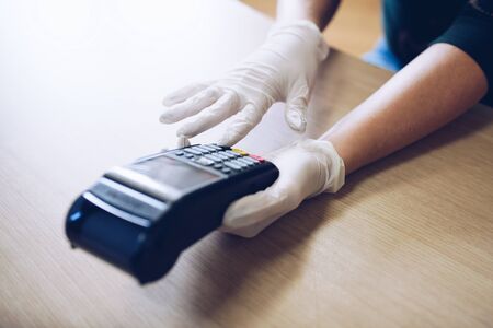 Woman gives the terminal for non-contact card payment.She wears protective gloves.