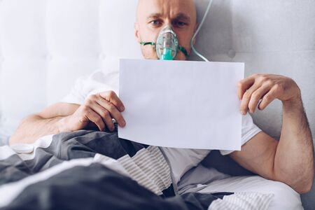 Coronavirus sick patient breathing through oxygen mask and holding empty cardの写真素材