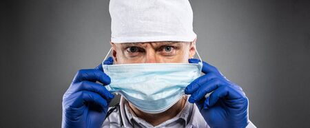 Medic doctor in white suit, protective gloves and medical mask holding card with message stay at homeの写真素材