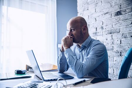 Worried confused man in shirt working on laptop computerの写真素材