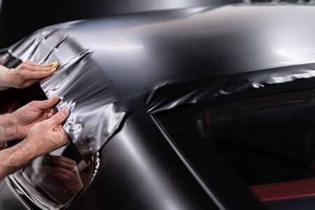 Man worker in car detailing studio applying color changing vinyl foil on car.の写真素材