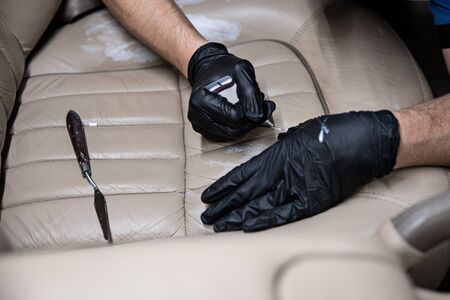 Worker of car detailing studio cleaning, painting and renovating leather car seatの写真素材
