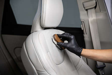 Man car detailing studio worker cleaning car leather seat with a brush.の写真素材
