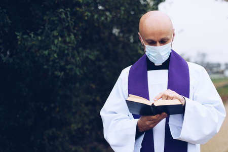 Priest in a medical mask reading holy bible.の写真素材