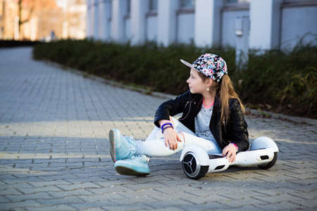 A 10-year-old girl in a flower cap sits with hers hoverboard.の写真素材