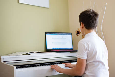 A young boy plays the digital piano with sheet music from his laptop.の写真素材