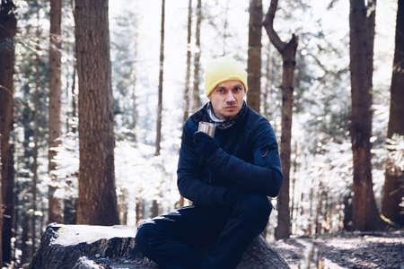 A tourist sitting on a tree stump in the forest holding a hot cup of teaの写真素材