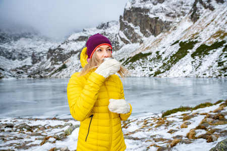 A cold woman tourist is drinking hot tea in a beautiful mountain landscape.