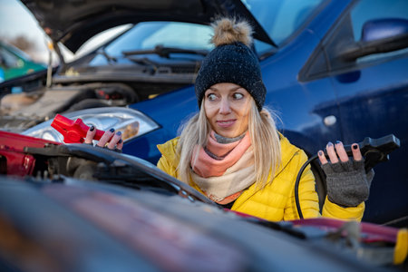 Irritated woman trying to start broken car with jumper cables.