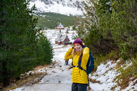 Smiling blond woman hiker in a yellow down jacket with a backpack spends his free time in the beautiful mountains.の写真素材