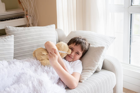 The sick boy is lying on the sofa hugging his teddy bear.の写真素材