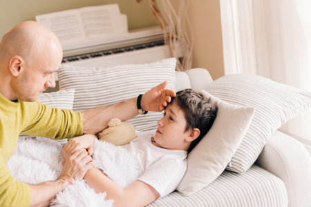 A caring single father takes the temperature of his sick son.の写真素材