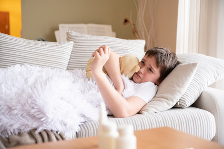 Sad sick boy is lying on the sofa hugging his teddy bear.の写真素材