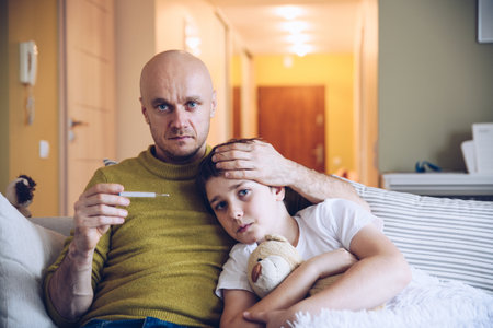 A caring single father hugs his sick son, measures his temperature.の写真素材