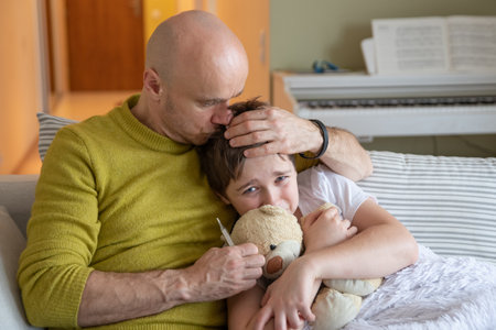 Lonely dad checks for fever. He hugs and kisses his sick son.の写真素材