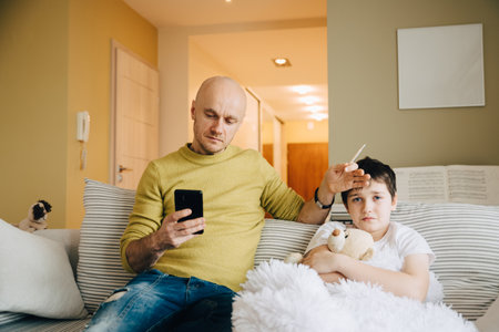 A single father takes the temperature of his sick son and calls the doctor.の写真素材