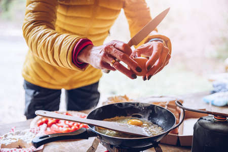 Woman preparing delicious tourist breakfast on the camping. Frying scrambled eggs outdoors.の写真素材