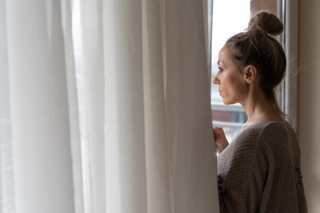A sad woman is looking out the window. Winter depression.