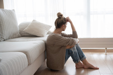 A depressed woman is sitting on the floor in the living room.の写真素材