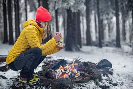 Young attractive blonde in a yellow jacket is eating canned food in the woods by the fire.の写真素材