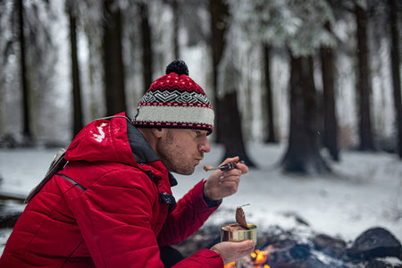 Handsome Man in a Red Jacket is holding an open can of canned food by the fire.の写真素材
