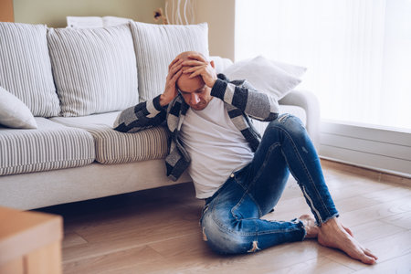 A worried man is sitting on the floor holding his head.の写真素材