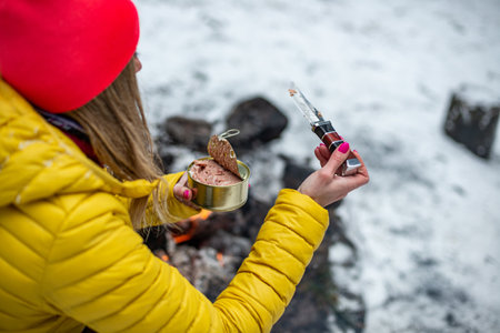 A woman in a yellow jacket with canned food by a fire on a mountain trail.の写真素材