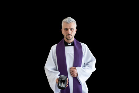 Handsome catholic priest holding credit card terminal. Church and moneyの写真素材