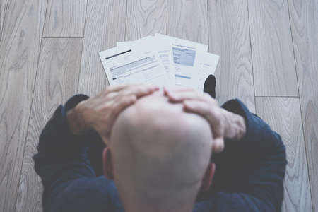 Desperate man sits on the floor. There are bankruptcy documents on the floor.の写真素材