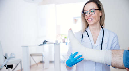 Smiling female doctor bandaging patients leg. Broken leg.の写真素材